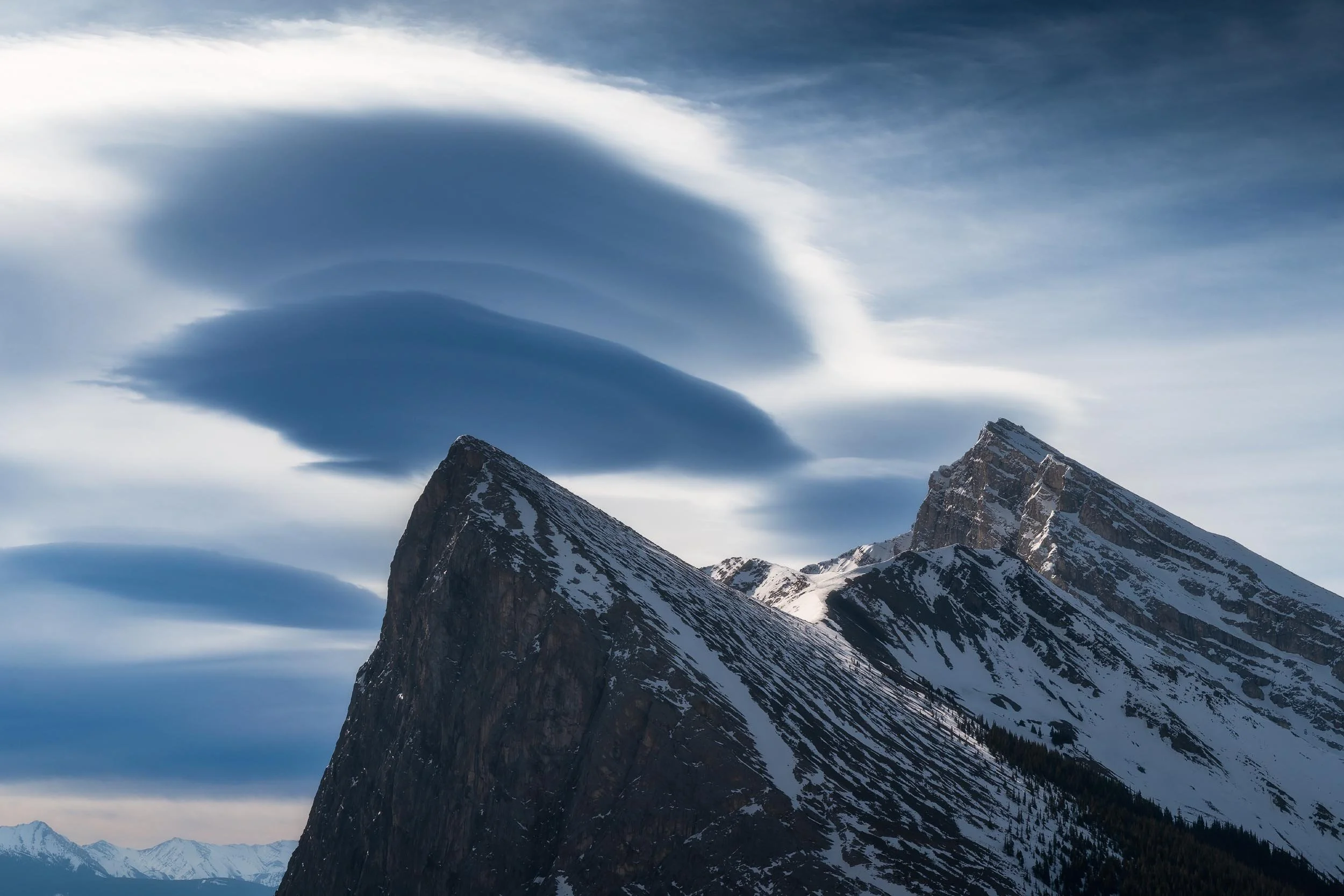 Snow-capped mountain peaks under a dramatic sky with large, swirling clouds.