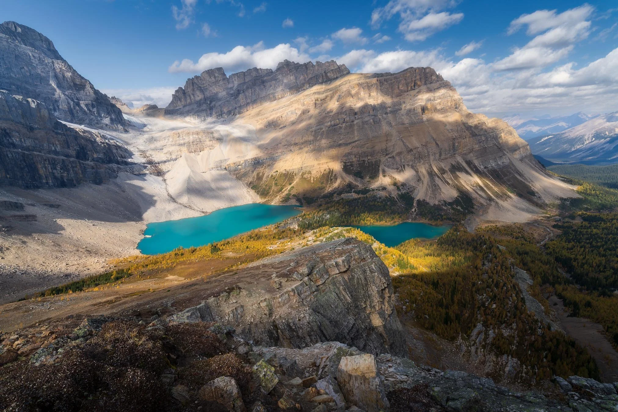 Scenic mountain landscape featuring rugged peaks, a glacier, and turquoise lakes surrounded by forested areas.