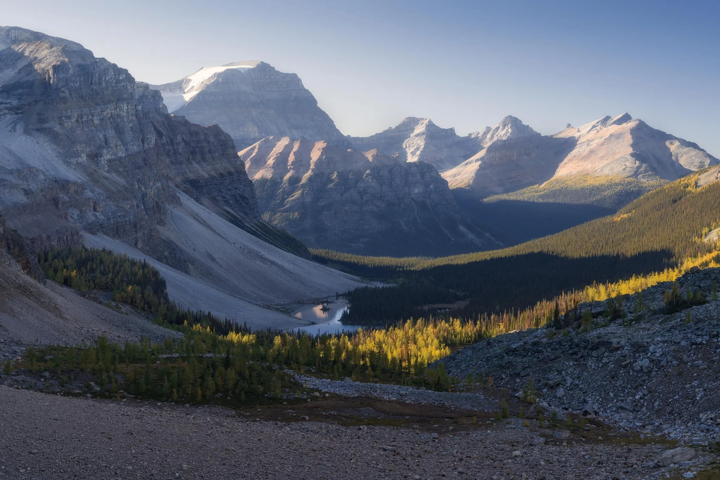 Scenic view of a mountain range with rugged peaks, a lake, and a forested valley under a clear sky.
