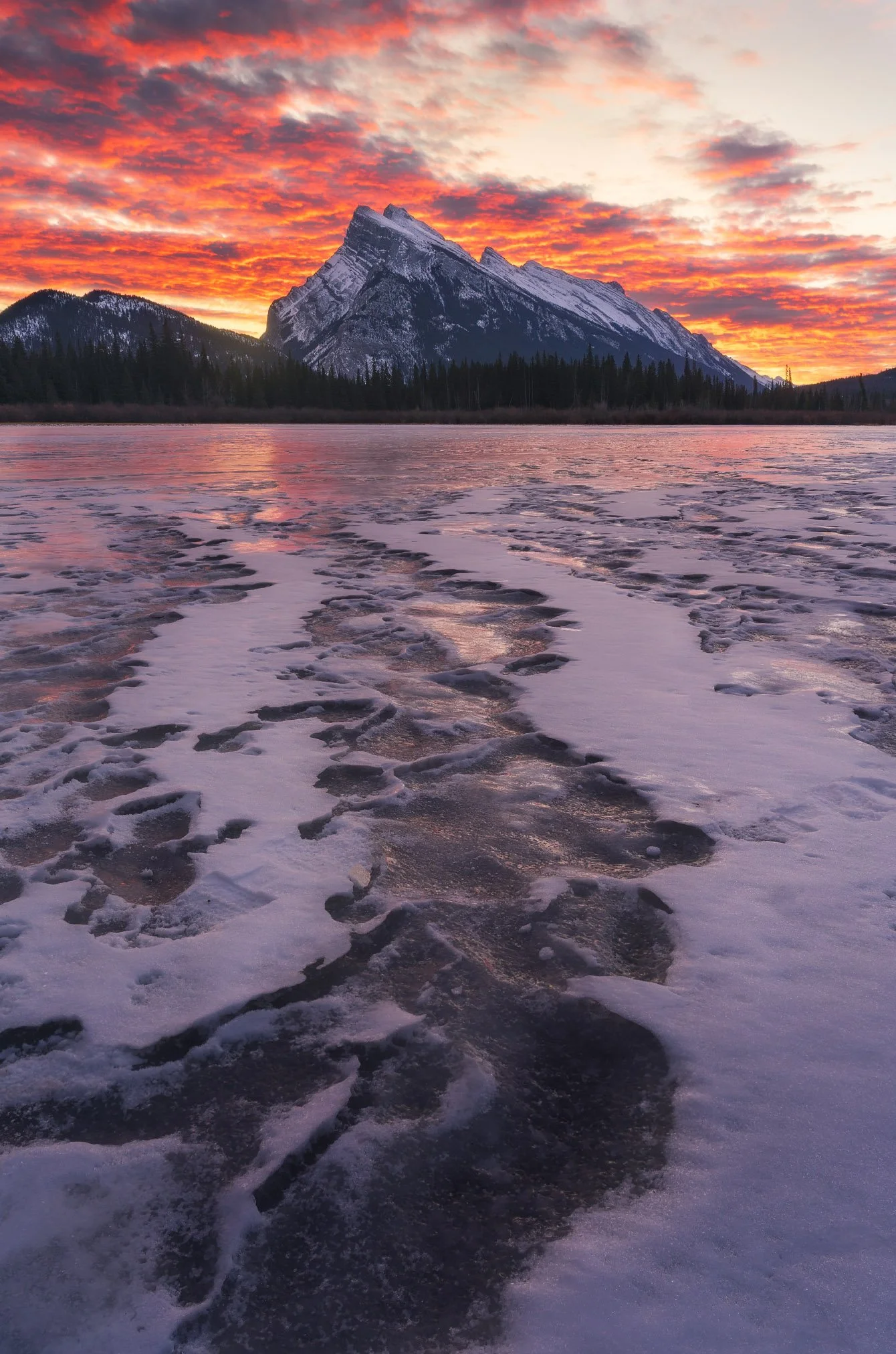 Snow and ice-covered surface leading to a mountain with snow on top, with a colorful sunrise sky in the background.