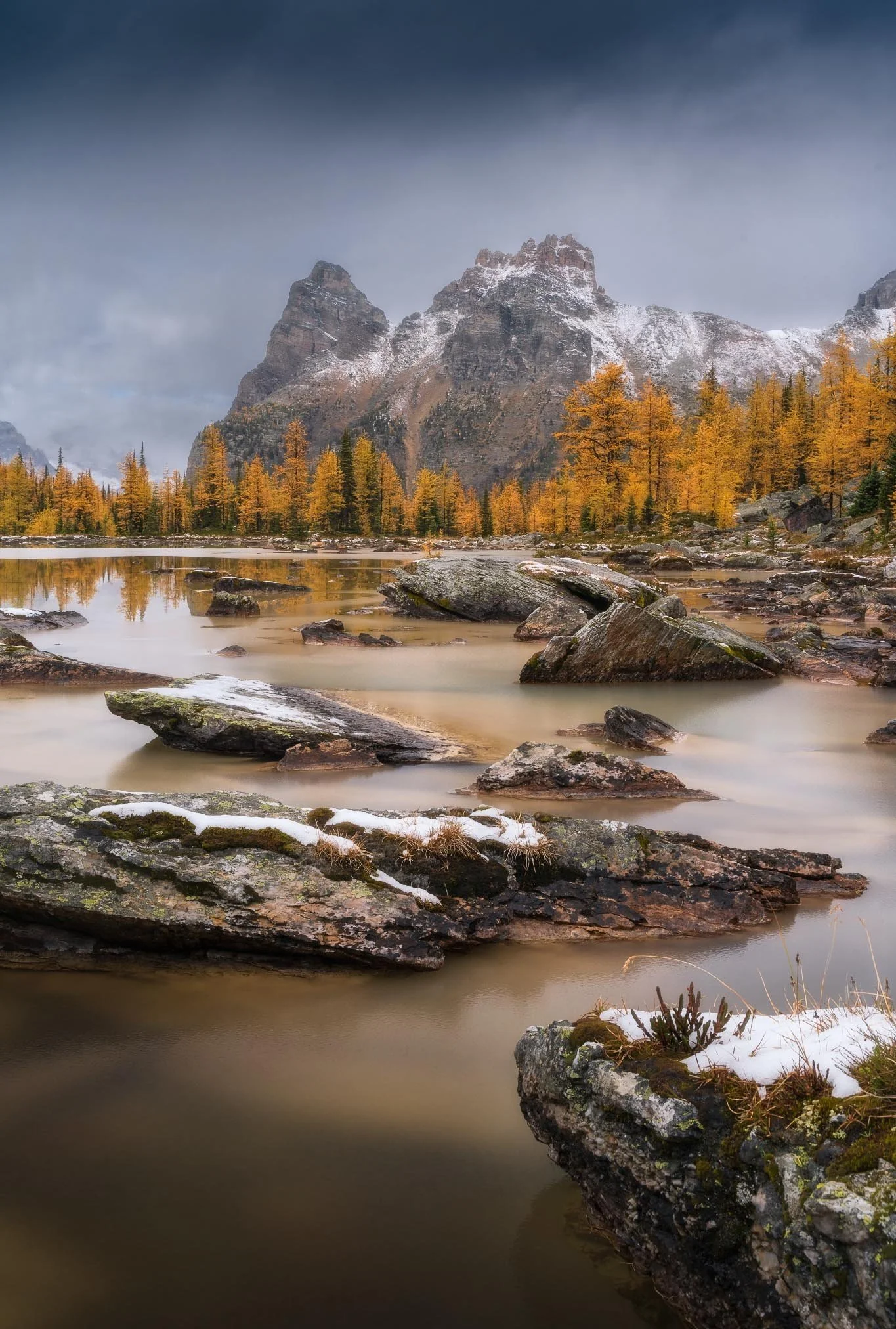Scenic mountain landscape with snow-capped peaks, a reflective river, and trees with autumn orange and yellow leaves.