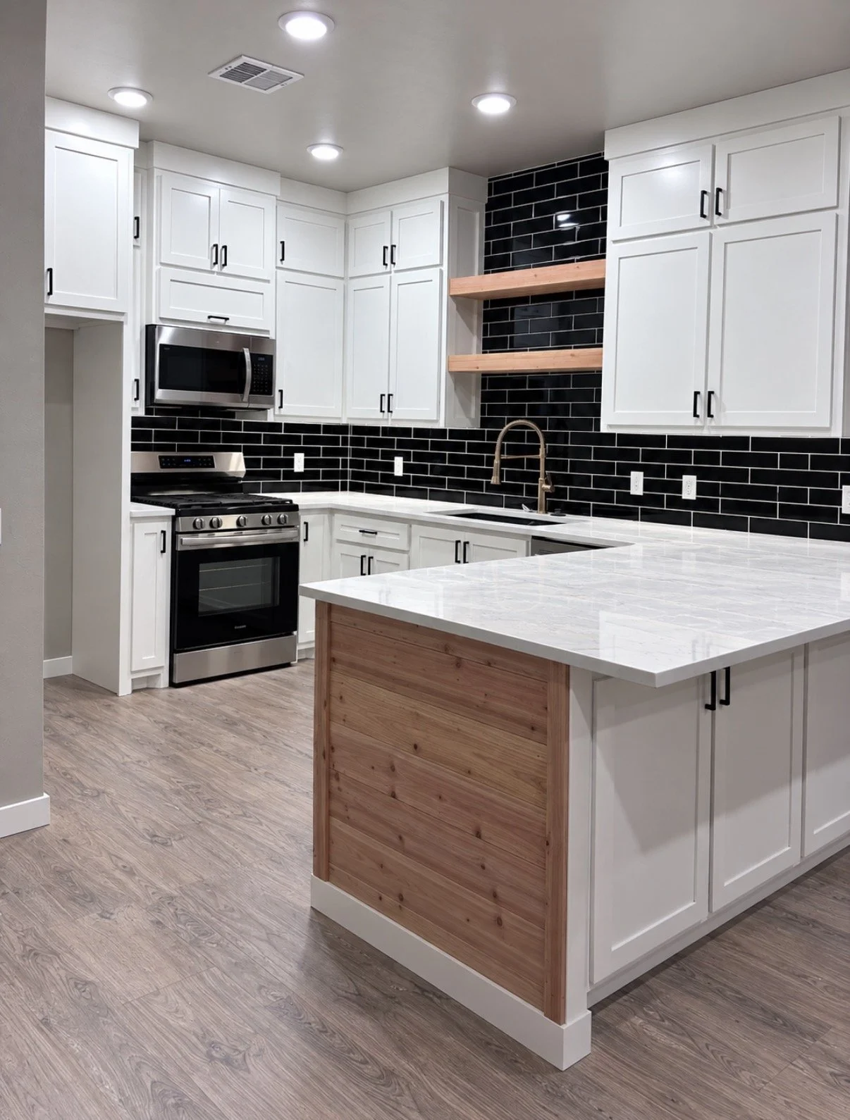 Modern kitchen with white cabinets, black tile backsplash, and wooden open shelves, featuring a marble countertop island and stainless steel appliances.