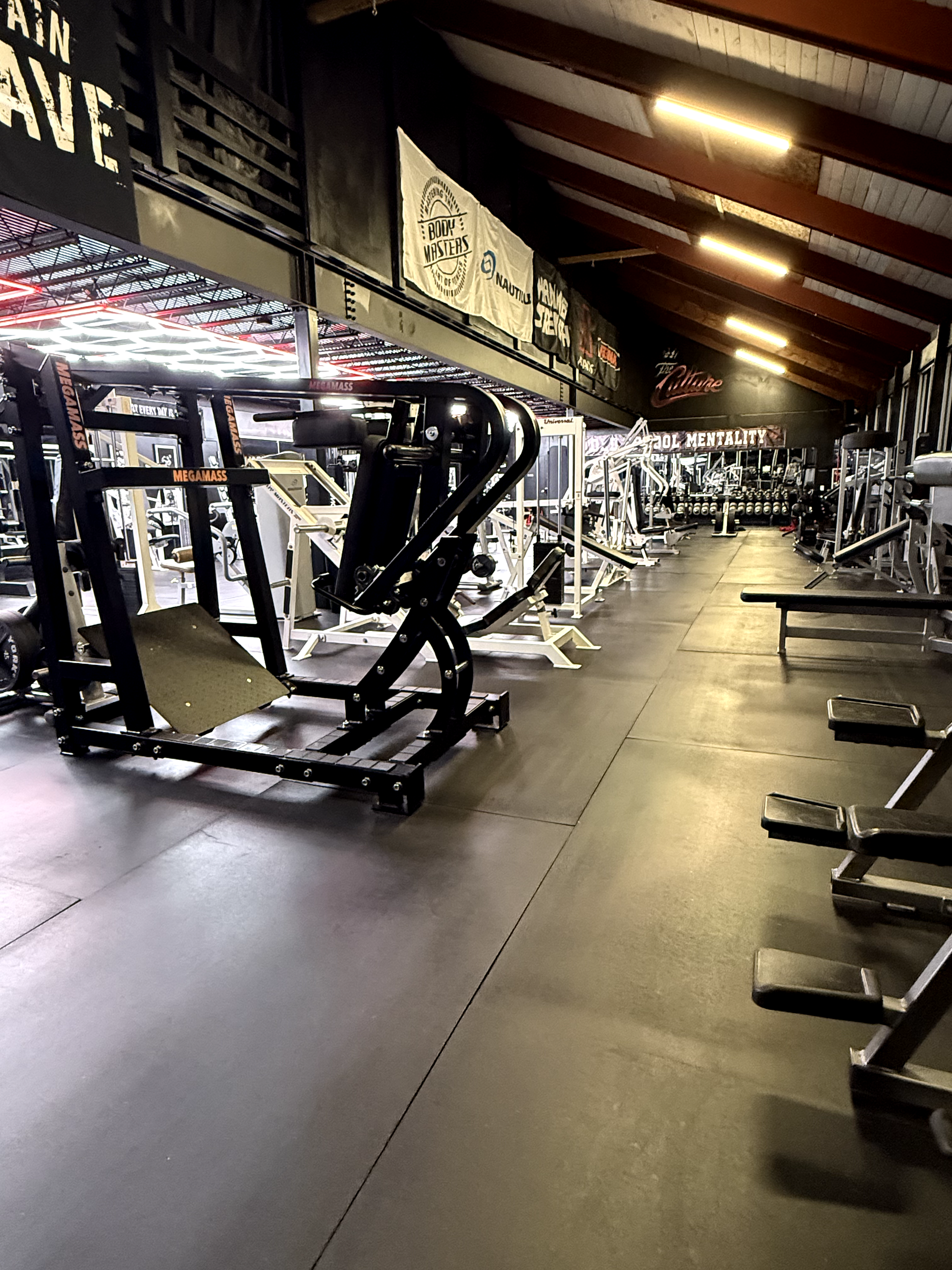 Indoor gym with various workout equipment, benches, and banners hanging on the wall.