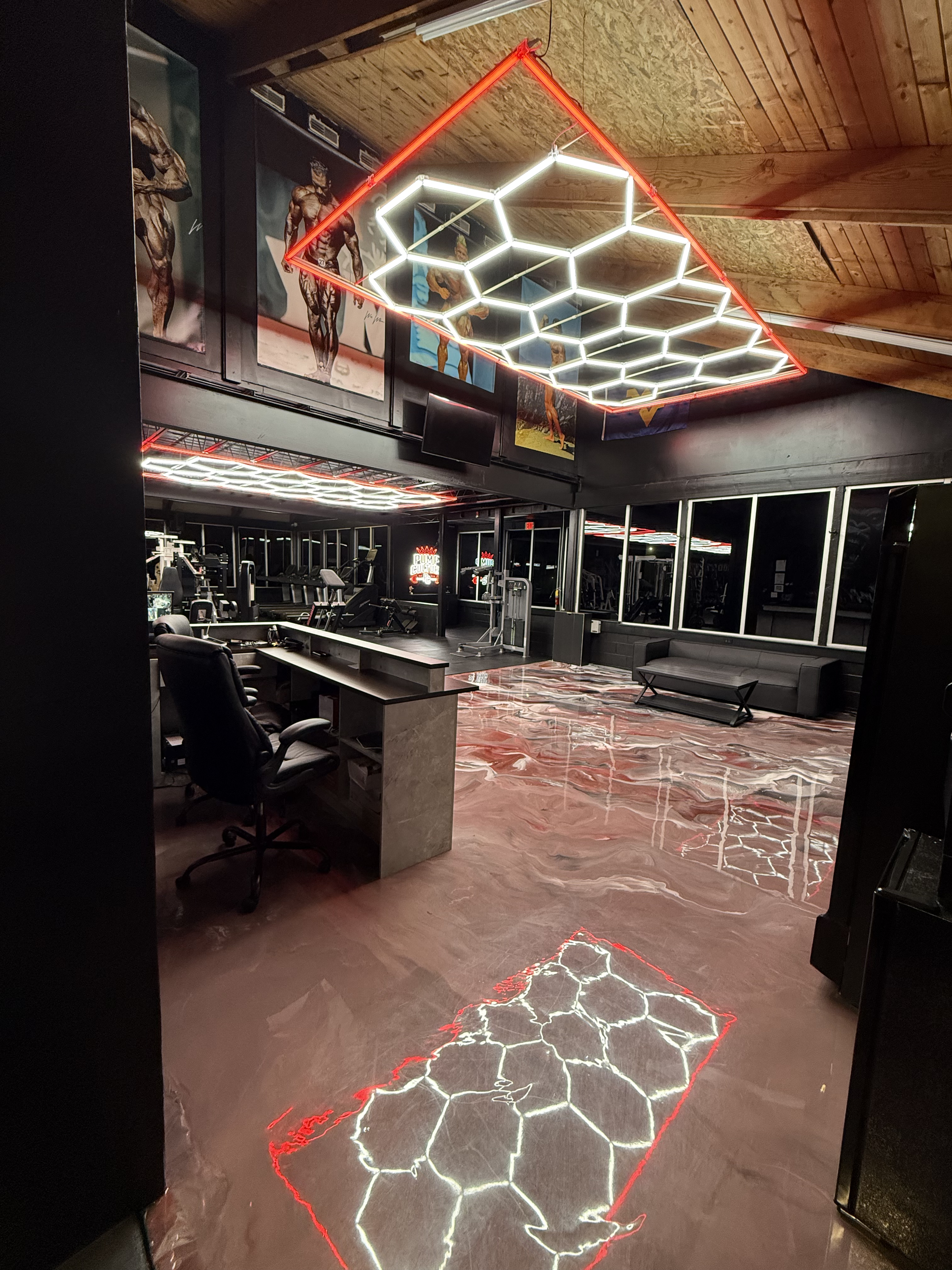 Neon lights form the outline of the state of Texas with a honeycomb pattern inside, located in a gym with posters of bodybuilders on the wall.