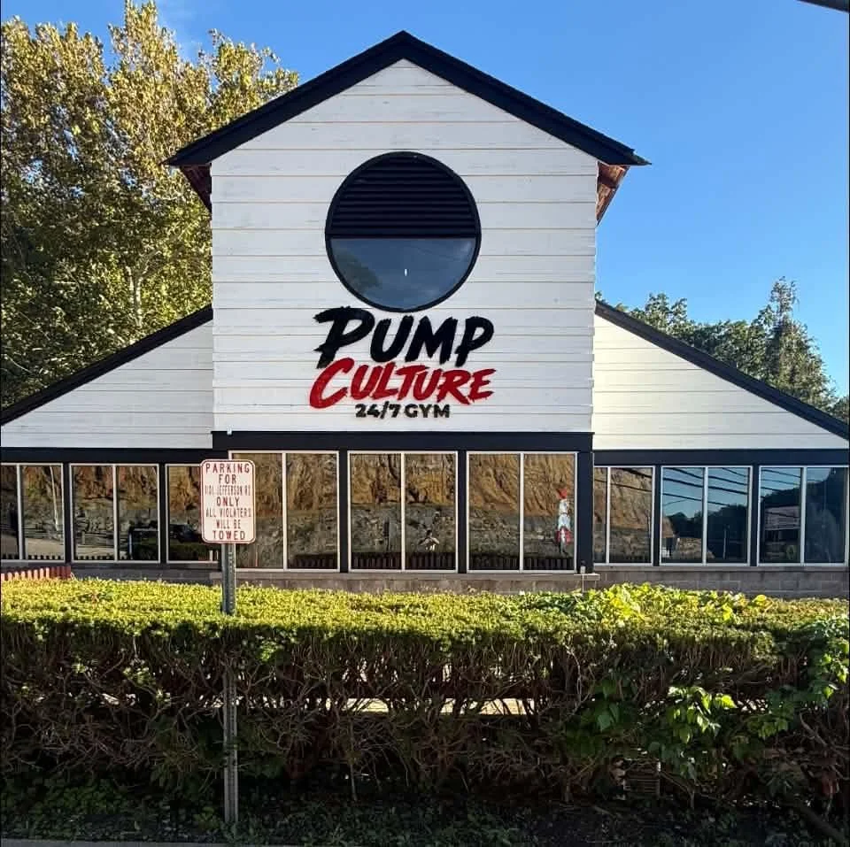 Building with sign reading 'PUMP CULTURE 24/7 GYM' and a parking sign in front.