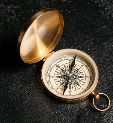 A gold pocket compass with an open lid, resting on a black textured surface.
