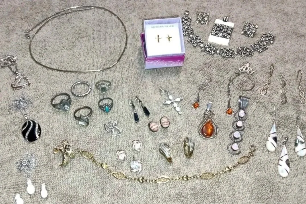Collection of jewelry including necklaces, rings, earrings, bracelets, and a pair of cross earrings in a purple box, laid out on a beige surface.