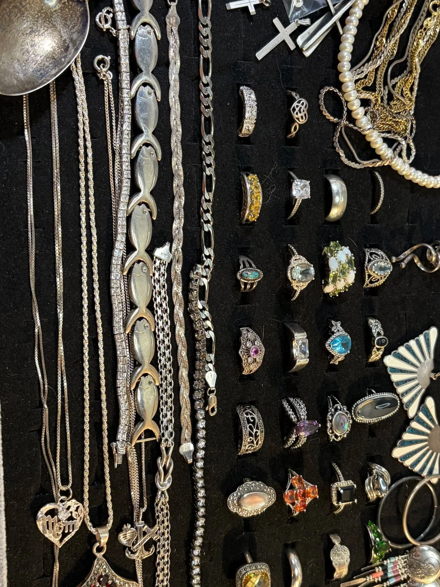 A collection of jewelry including necklaces, rings, earrings, and bracelets, displayed on a black background. The jewelry is mostly silver, gold, or adorned with gemstones and pearls.