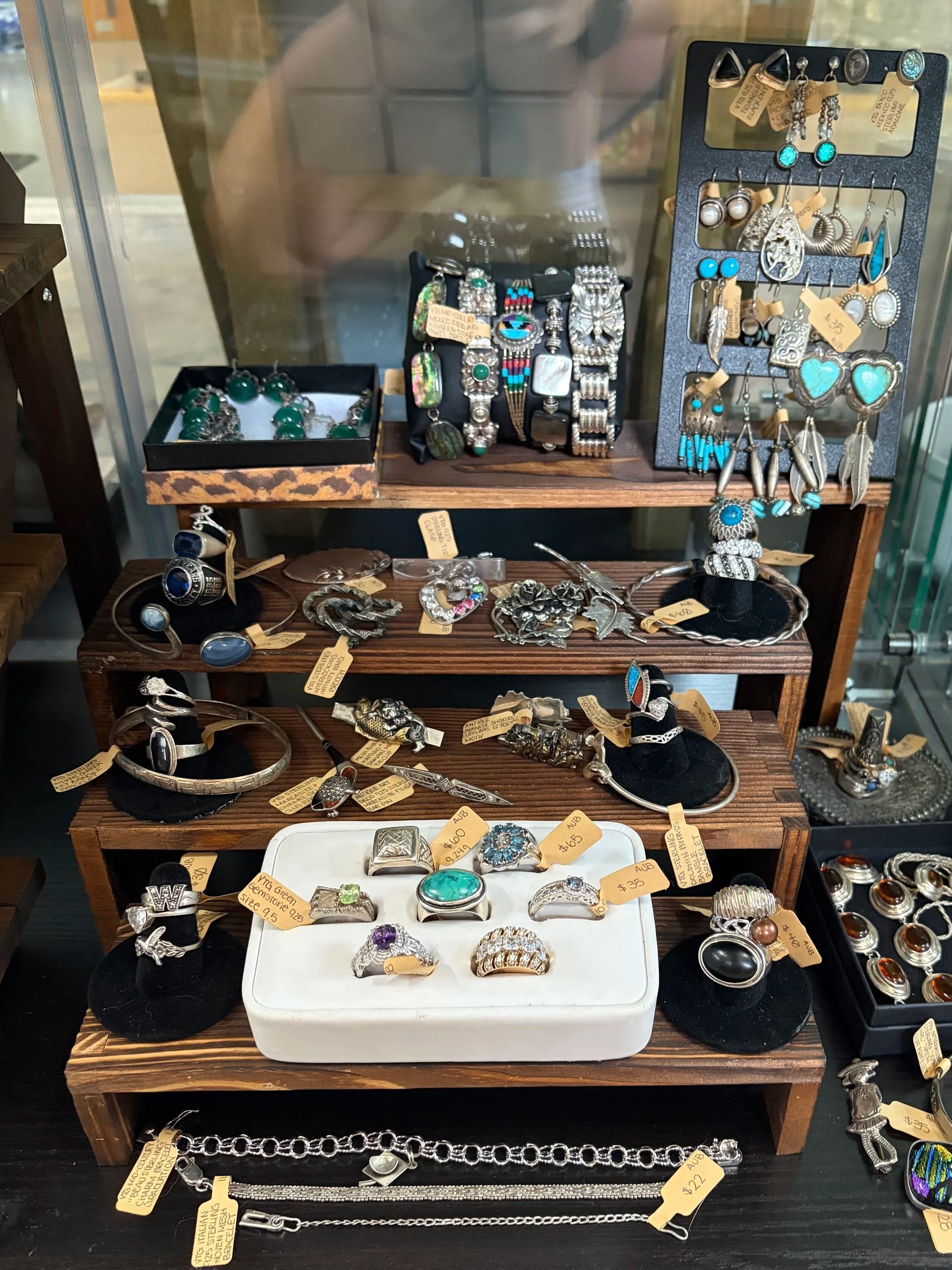A display case with various vintage jewelry and accessories, including rings, bracelets, earrings, and necklaces, mostly made of silver with turquoise accents, and some with price tags.