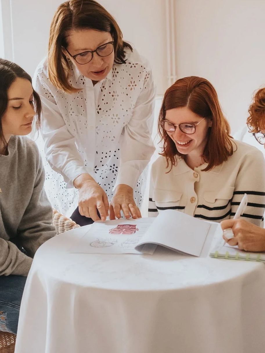 Groupe de femmes discutant autour d'une table avec des livres et des notes, dans une ambiance chaleureuse.