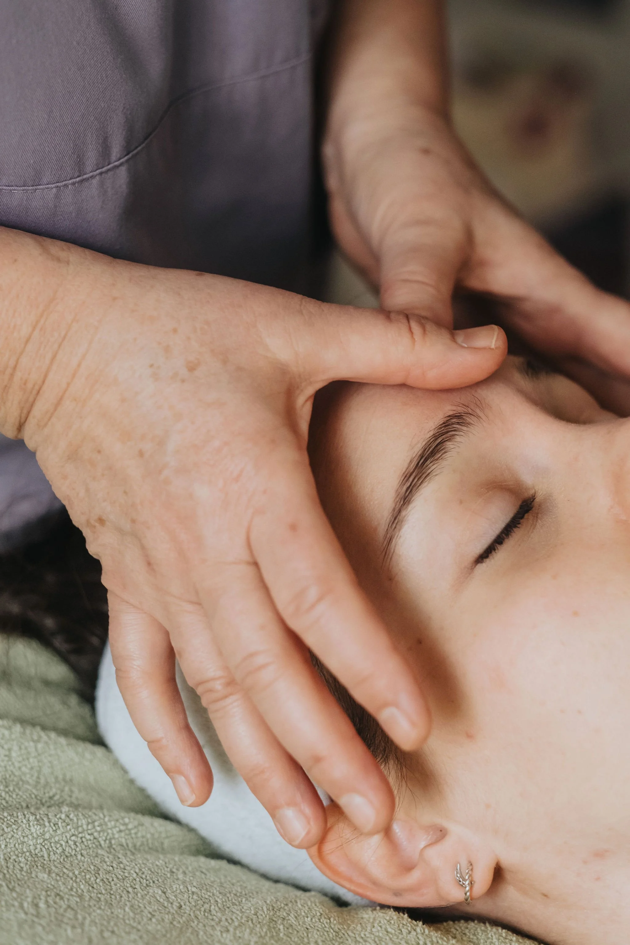 Mains de la praticienne posées sur le front d'une cliente pour un massage doux du visage.