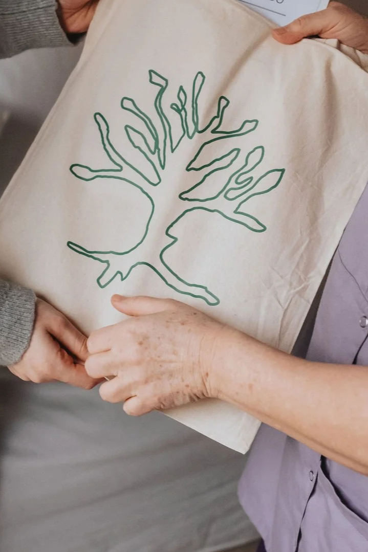 Deux personnes tiennent un sac en toile avec un dessin d'arbre stylisé tracé en vert.