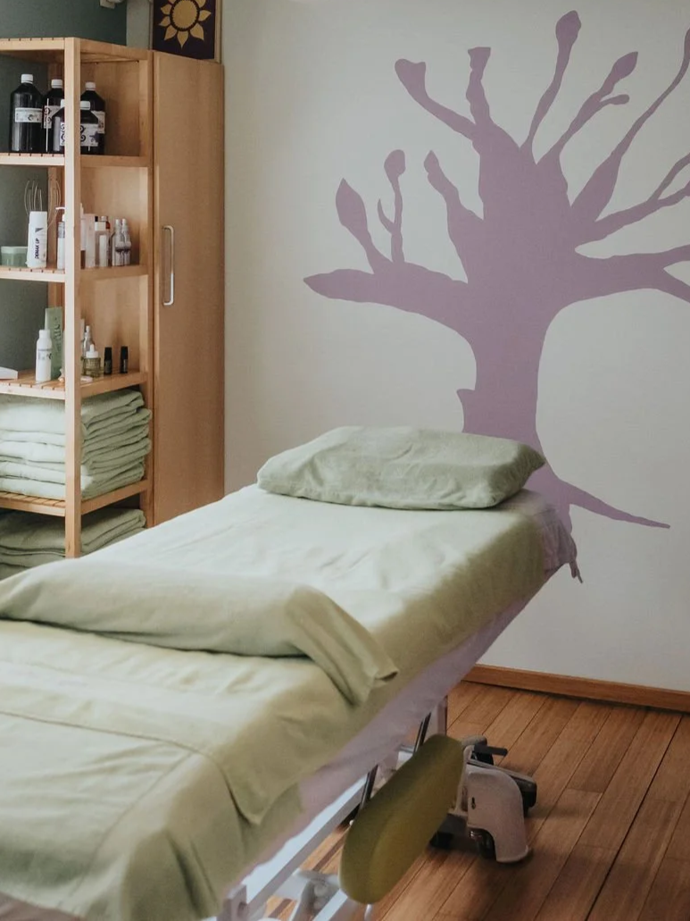 Table de massage dans le cabinet, avec une peinture d'arbre au mur.