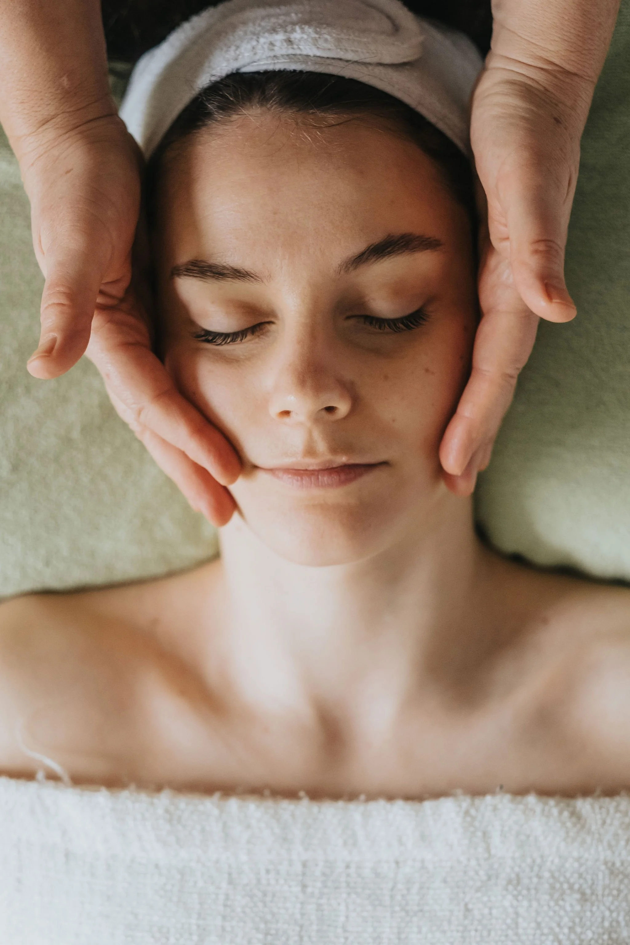 Massage du visage : les mains de la praticienne posées sur les joues d'une femme allongée, les yeux fermés