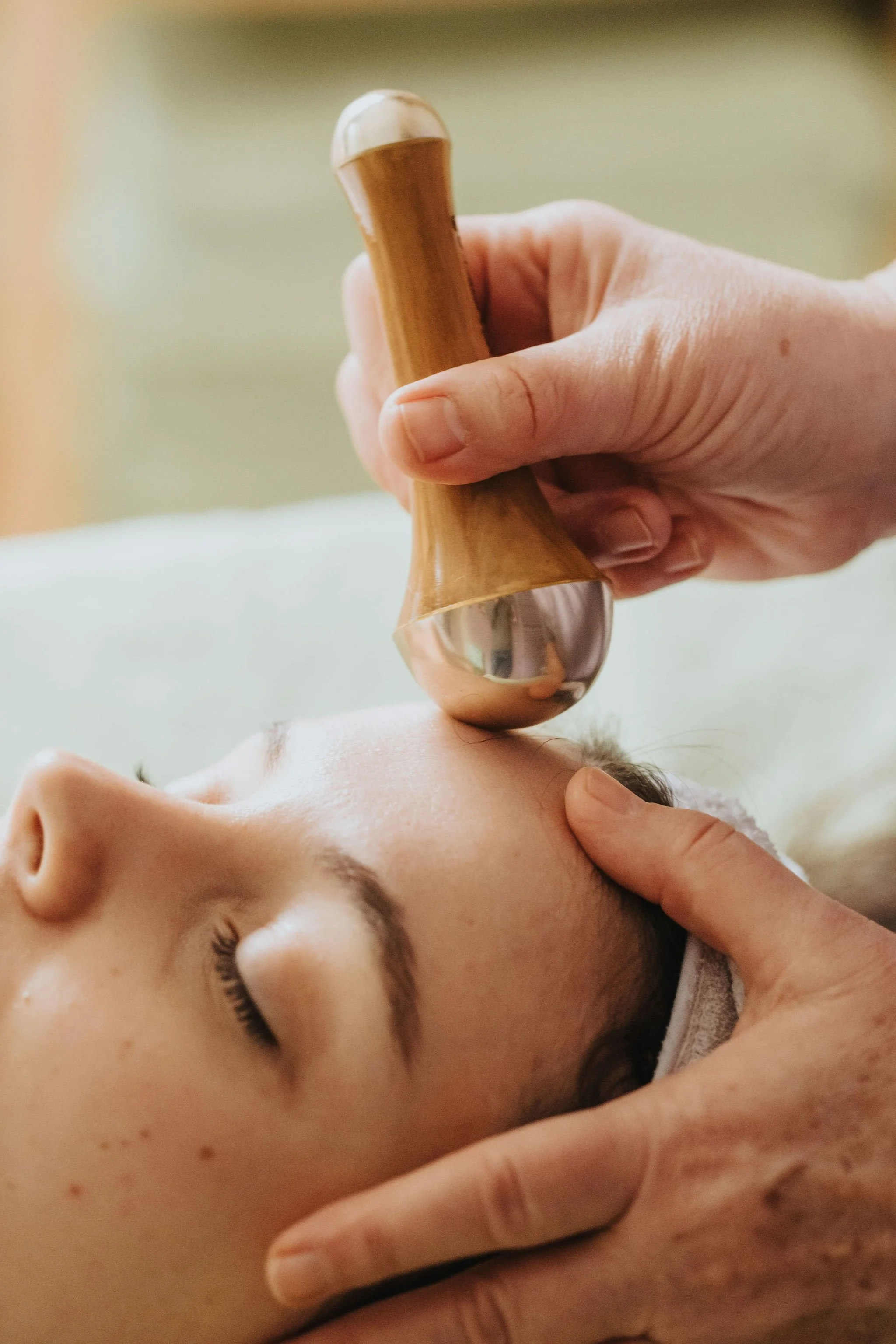 Outil Kansa Wand en bois et métal glissé sur le visage d'une cliente.