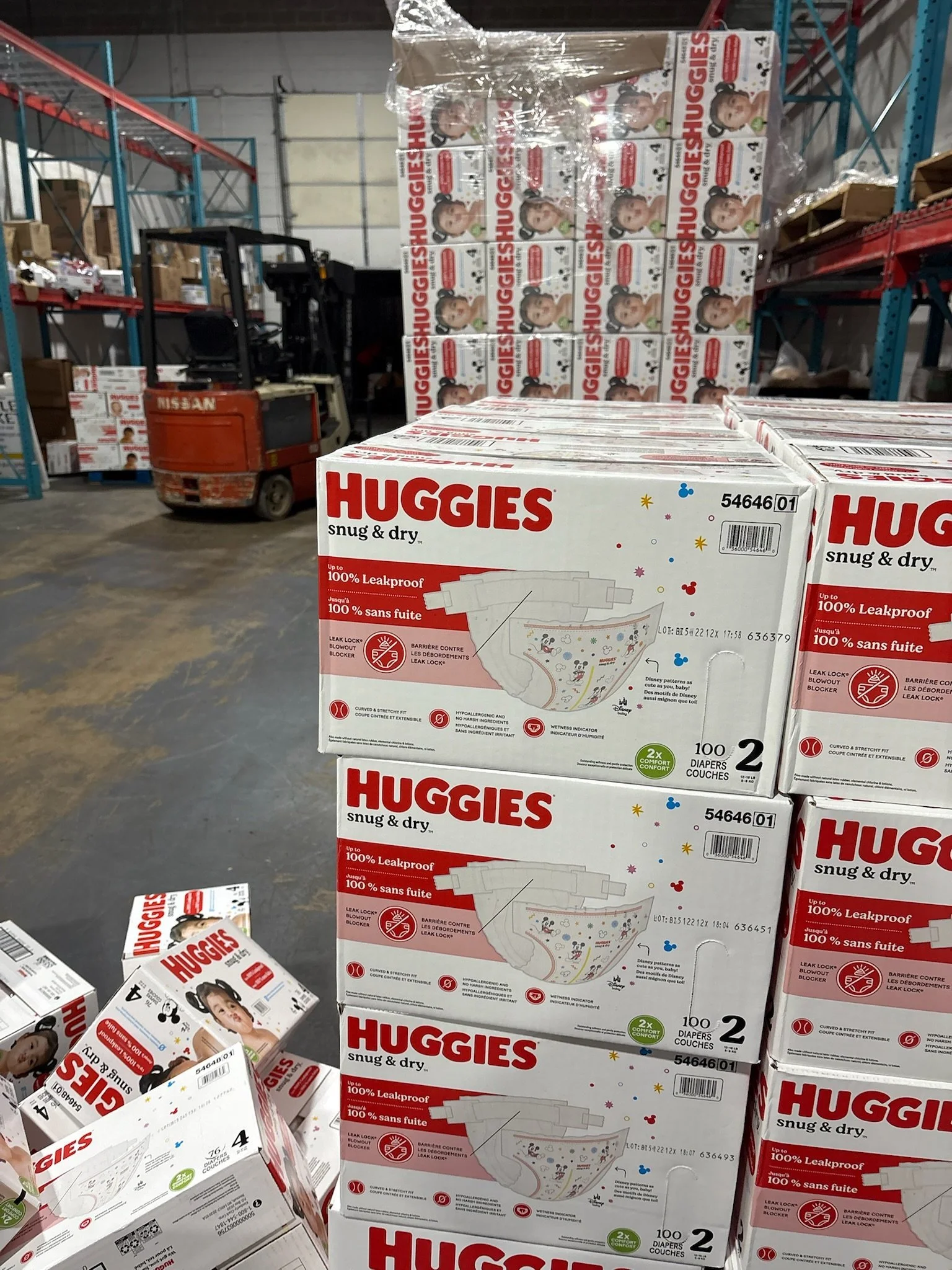 Boxes of Huggies Snug & Dry diapers stacked on a warehouse shelf, with a forklift nearby.