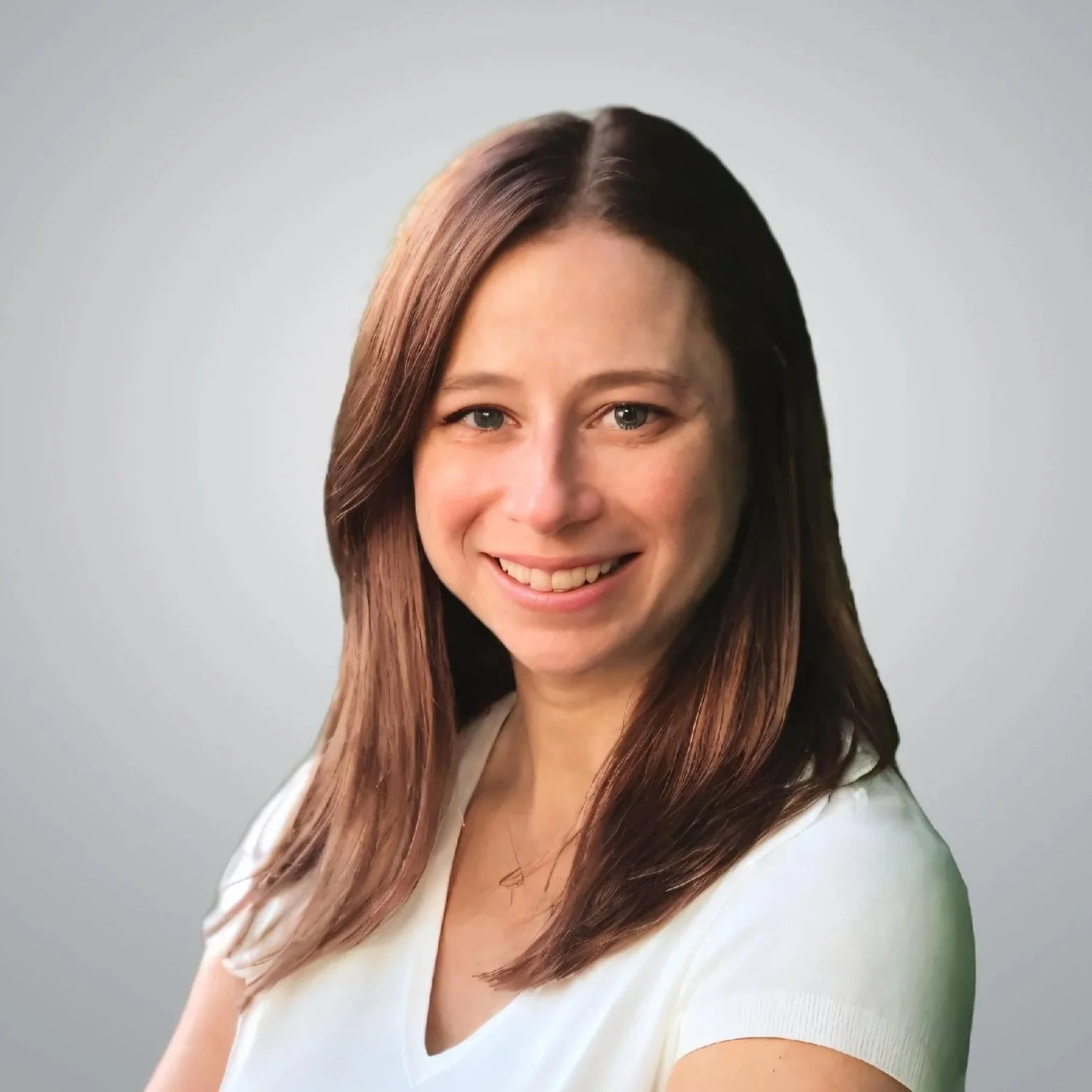 A woman with long brown hair and light skin, smiling, wearing a white top, against a neutral gray background.