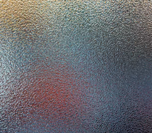 Close-up of textured, frosted or matte glass surface with a mixture of blue, gray, and red hues.