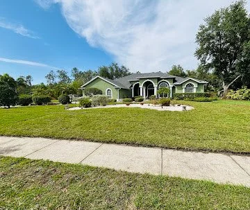 A large suburban house with a front lawn and sidewalk in Florida, under a partly cloudy sky.