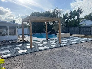 Backyard with an above-ground pool, a wooden pergola, and a patterned concrete patio. Fenced yard with trees and neighboring houses visible in the background.