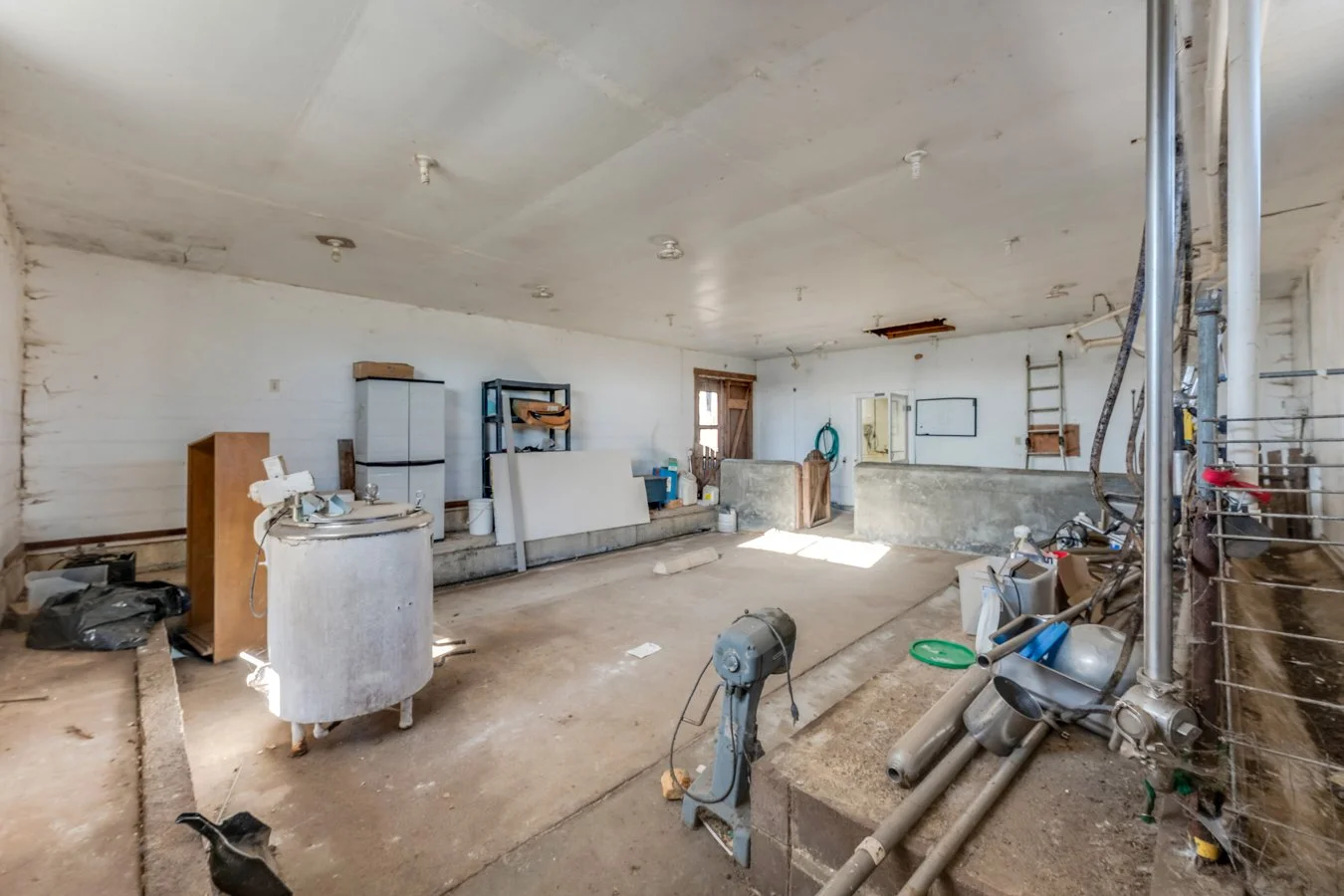Empty, unfinished room with construction materials, pipes, and tools scattered around.