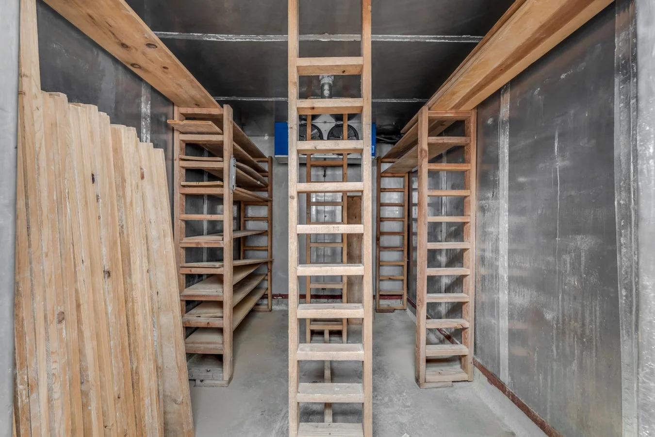 Empty wooden wine cellar with shelves on both sides and a central ladder for reaching higher racks.