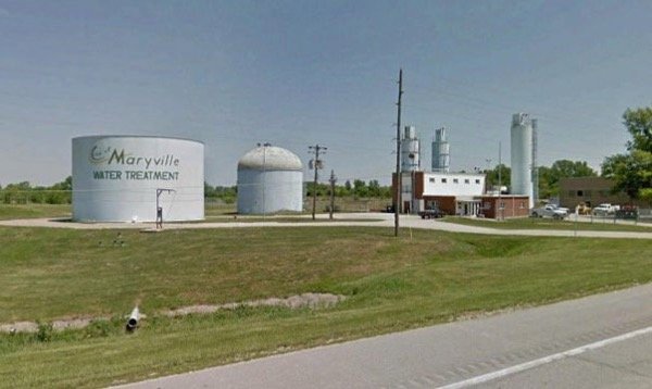 Water treatment plant with large storage tanks, a small building, and some utility poles over a grassy area.