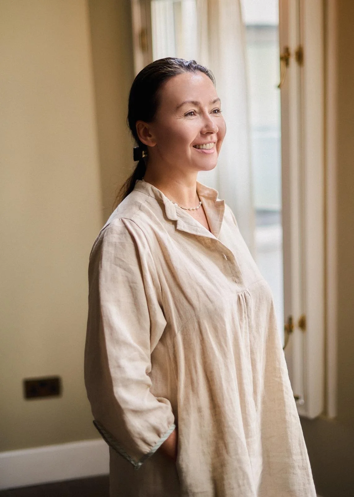 A smiling Nataliya Robinson with dark hair tied back wears a beige collared dress.