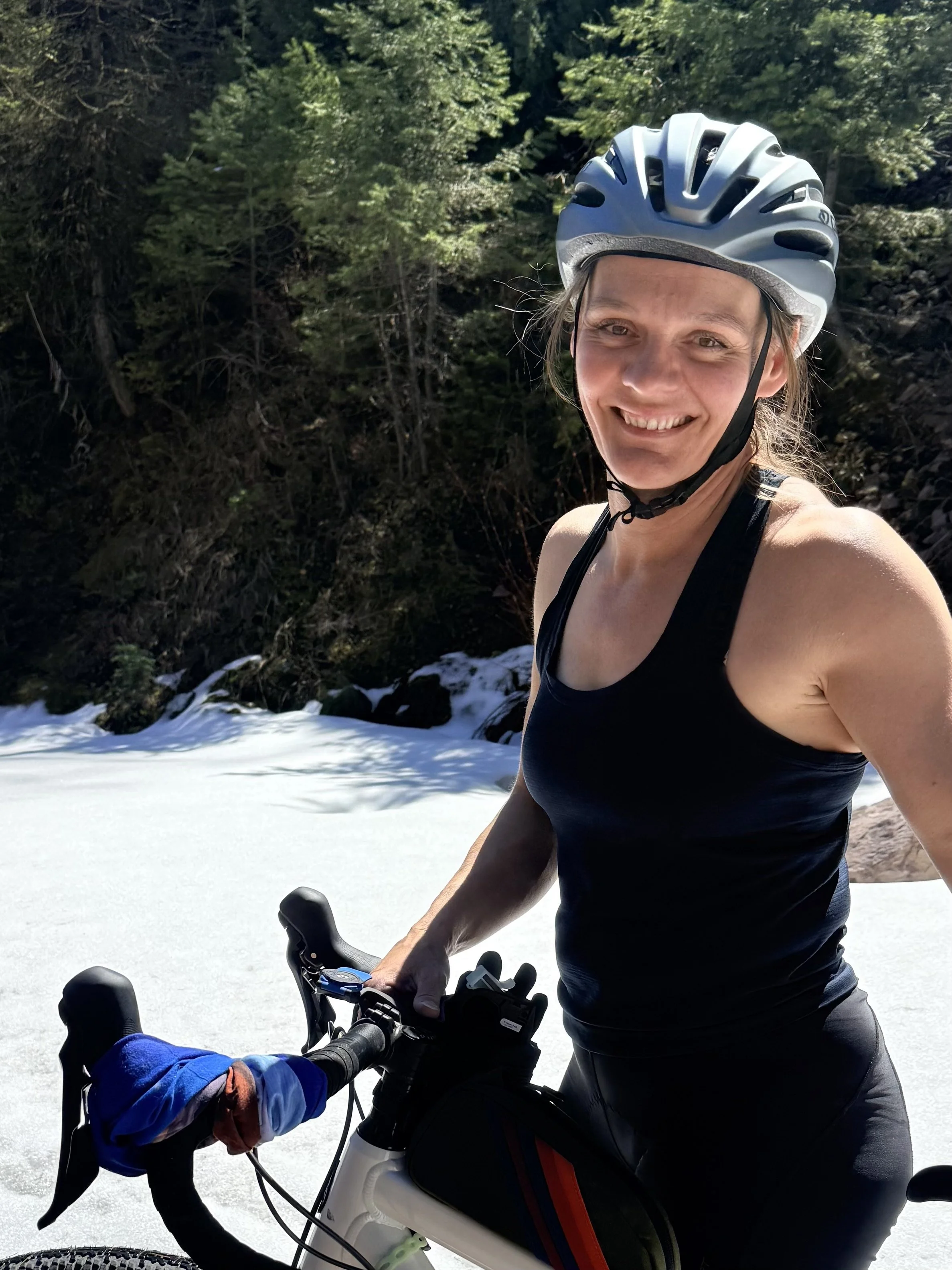LeeAndra with her bicycle on a snowy trail surrounded by trees.