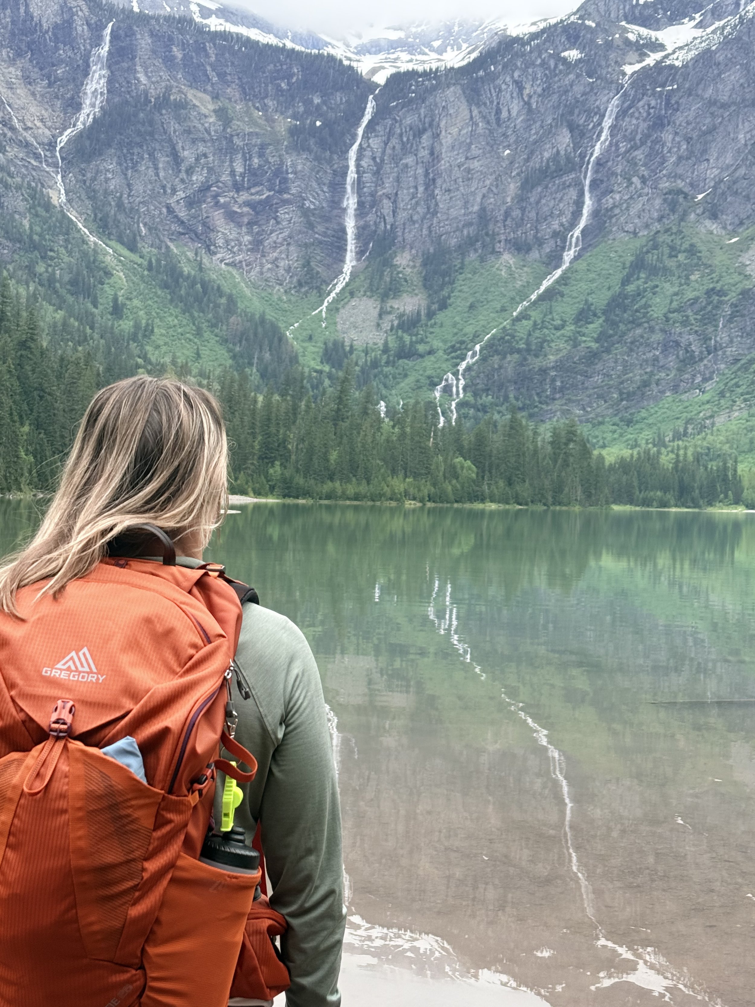LeeAndra overlooking an alpine lake surrounded by mountains and waterfalls.