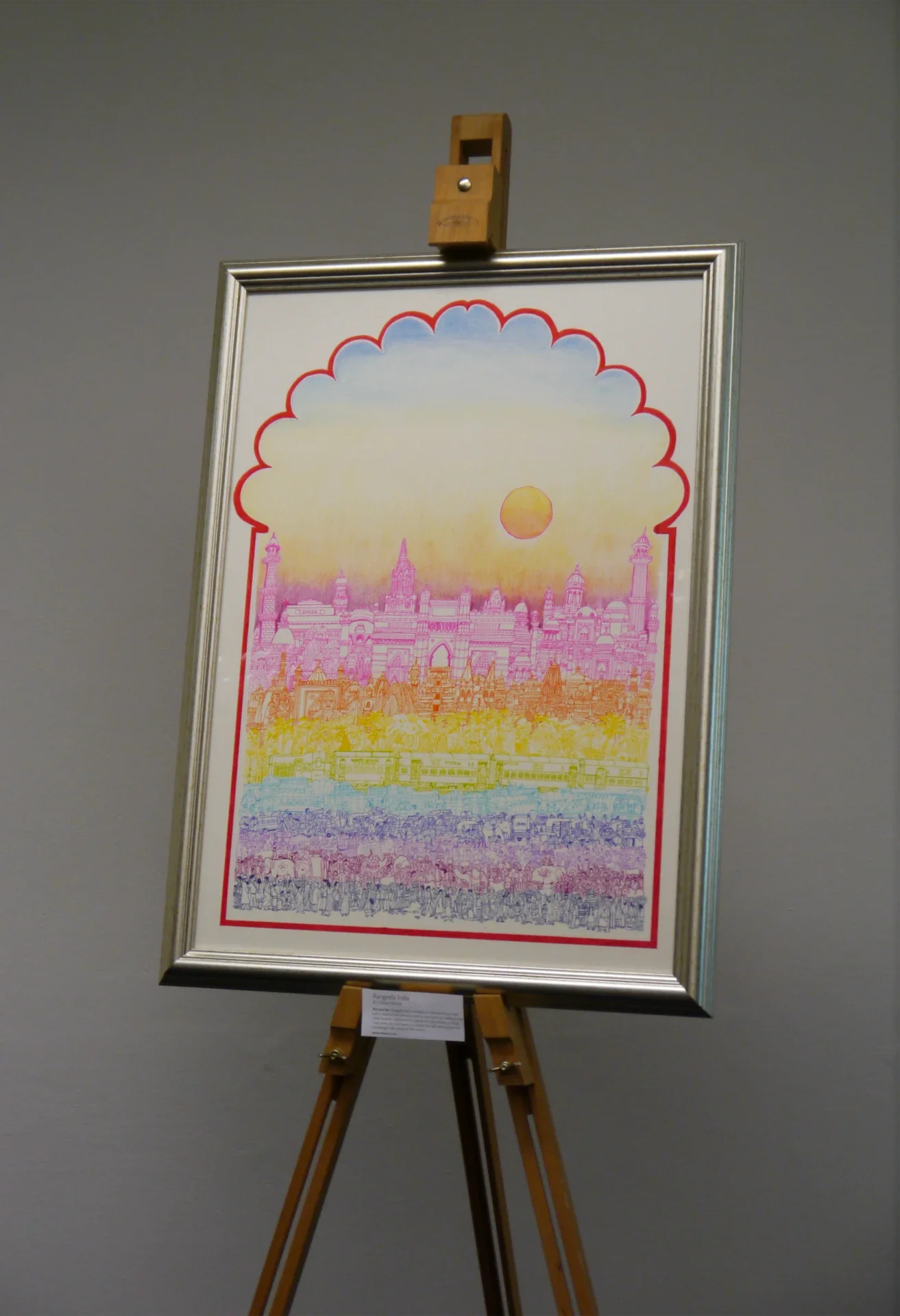 Framed original artwork on display at an exhibition easel, featuring an arched Indian cityscape in vivid gradient colors.