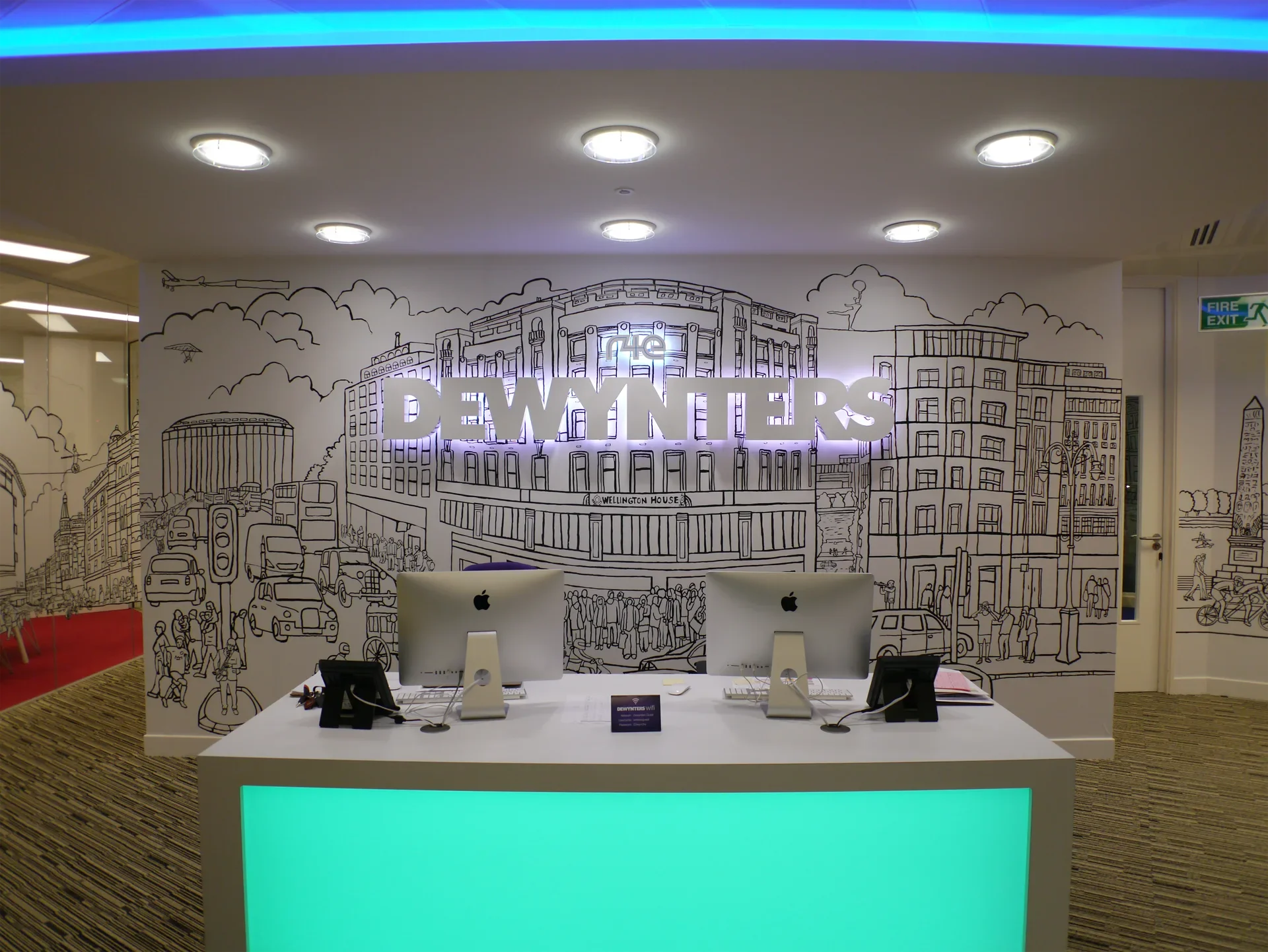 Main reception desk at Dewynter's London featuring the custom illuminated logo and full-wall cityscape mural.
