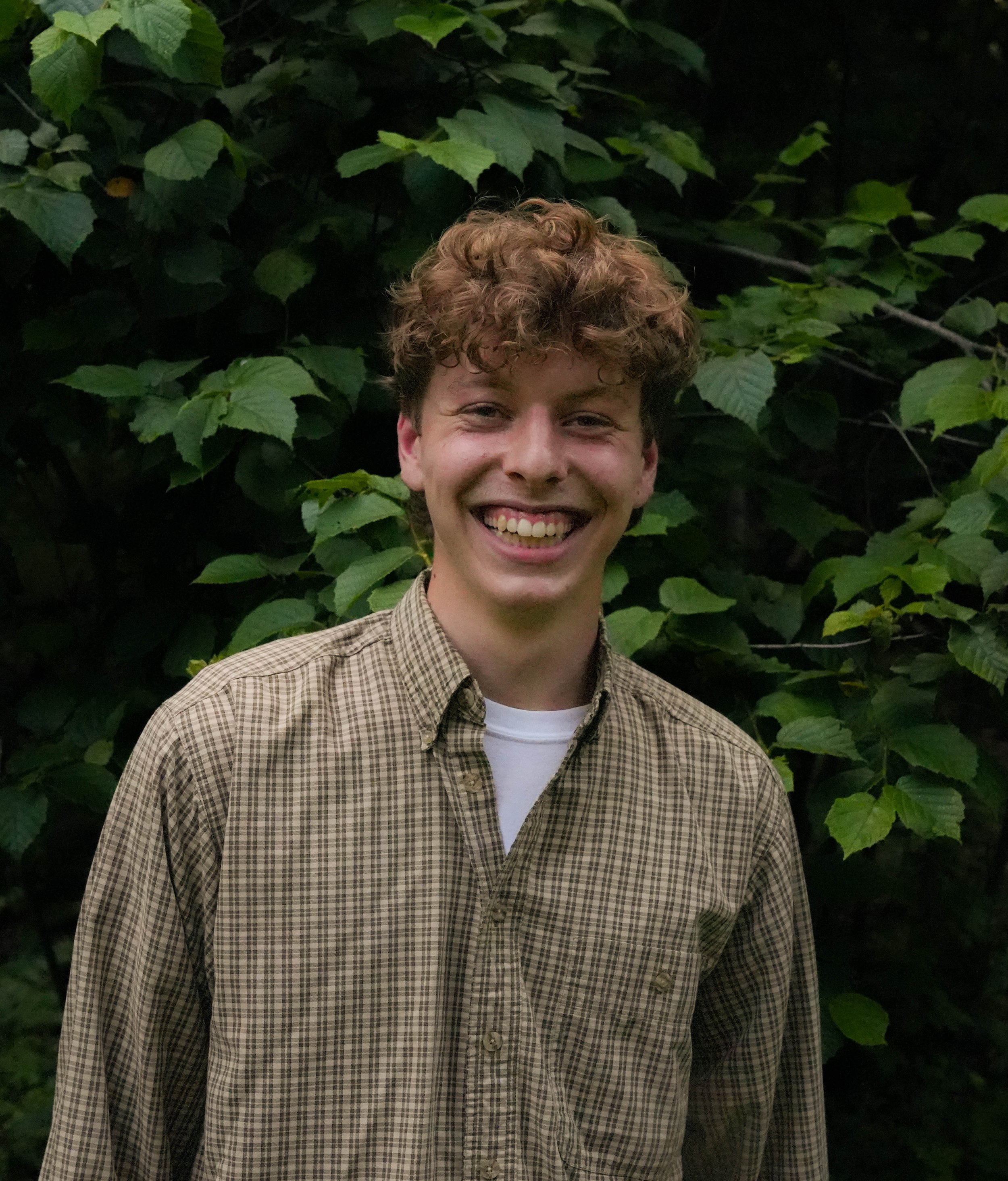 Portrait of Steven smiling in front of green leafy bushes.