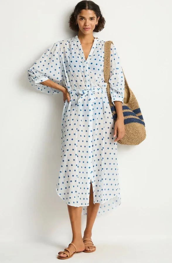 Model in a white and blue polka dot shirtdress carrying a straw tote