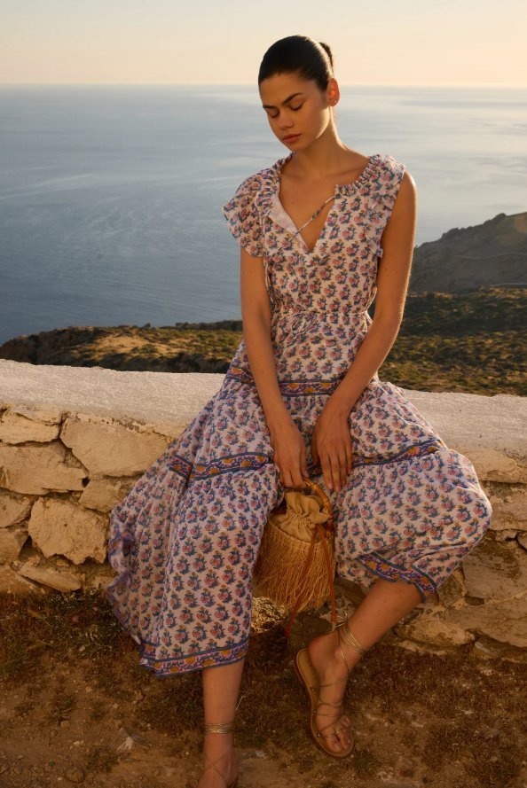 Model in a mauve block-print sleeveless maxi dress seated on a seaside stone wall