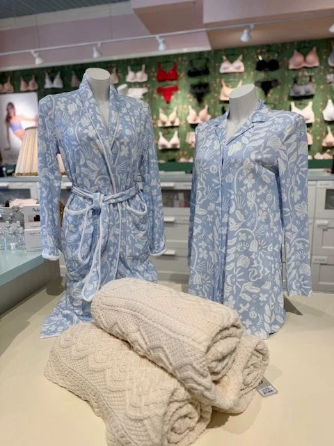 Blue and white print robe and pajama shirt displayed in the shop with folded cream cable-knit throws