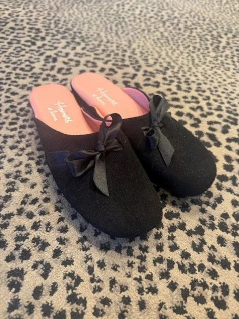 Black felt slippers with satin bows and pink lining on a leopard print rug