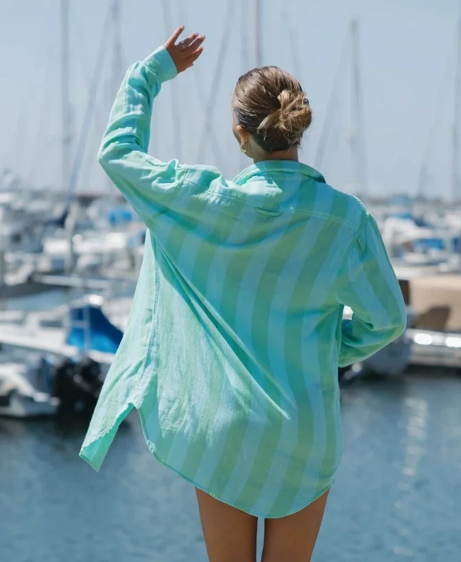 Back view of a model in an aqua striped oversized shirt at a marina