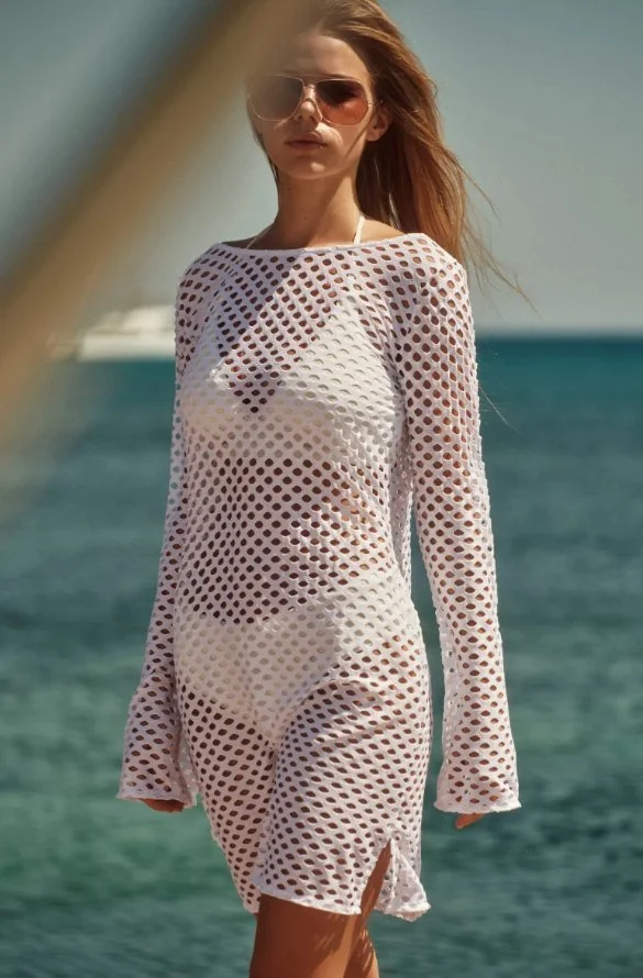Model in a white open-knit cover-up and sunglasses by the sea