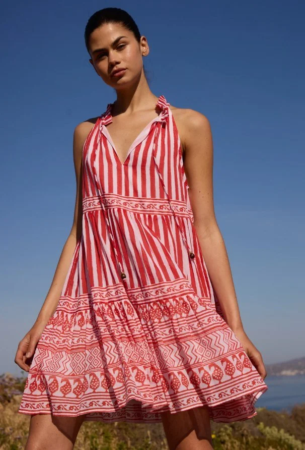 Model in a red and white patterned tiered halter dress by the sea