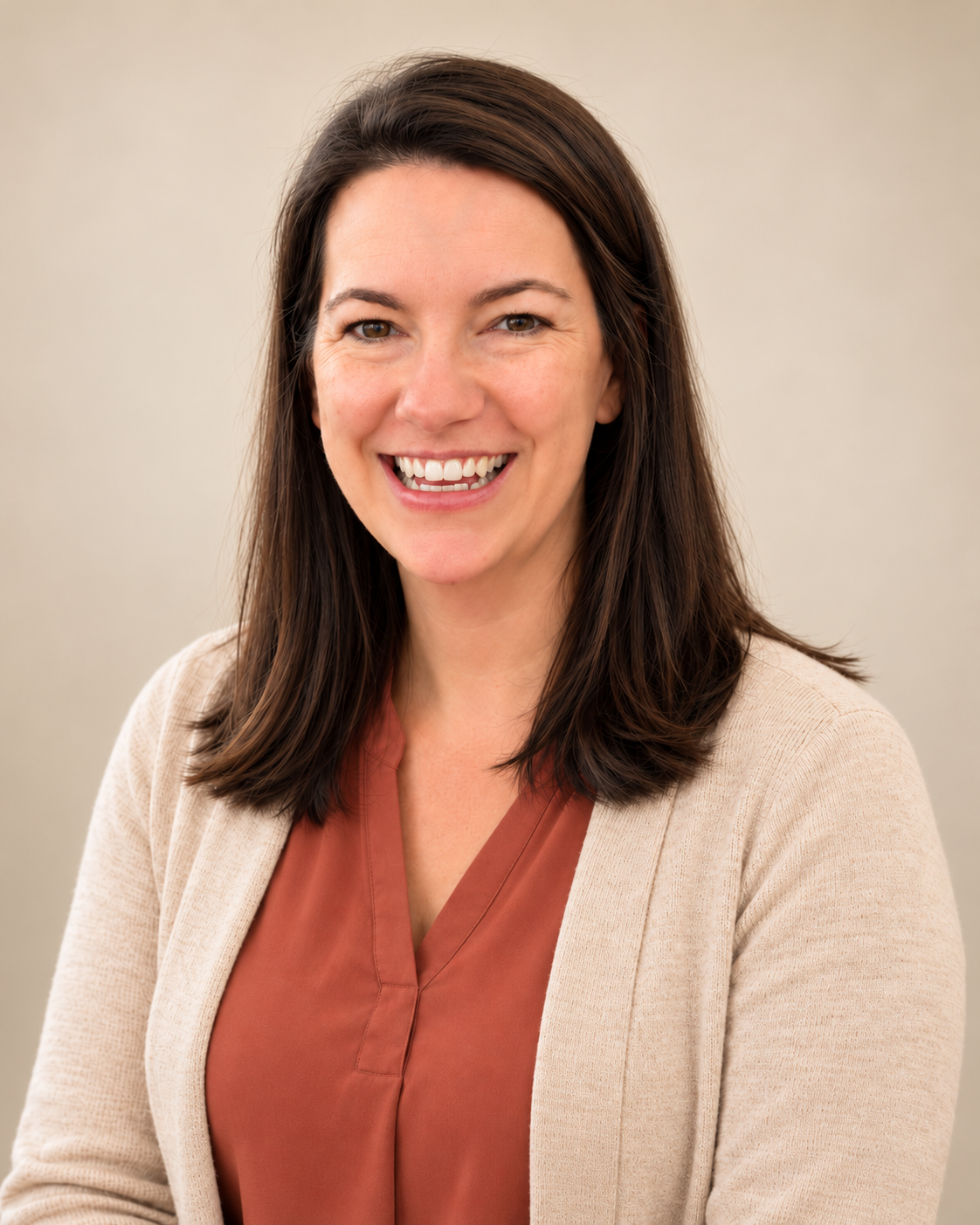 Kaitlin, an occupational therapist, smiles at the camera in a rust-colored blouse and cream cardigan against a warm neutral background.