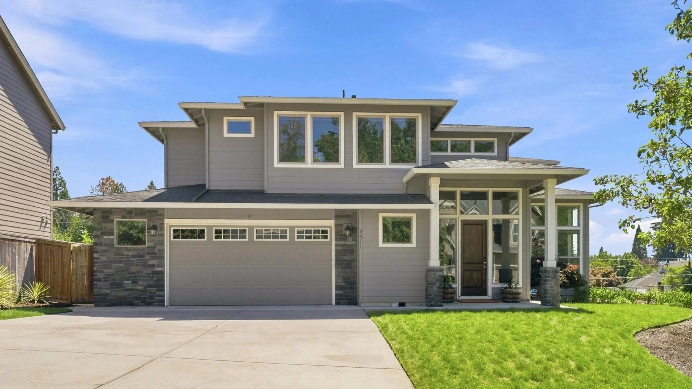 A modern two-story house with a gray exterior, large windows, a stone facade on the garage, and a well-maintained front yard with a green lawn.