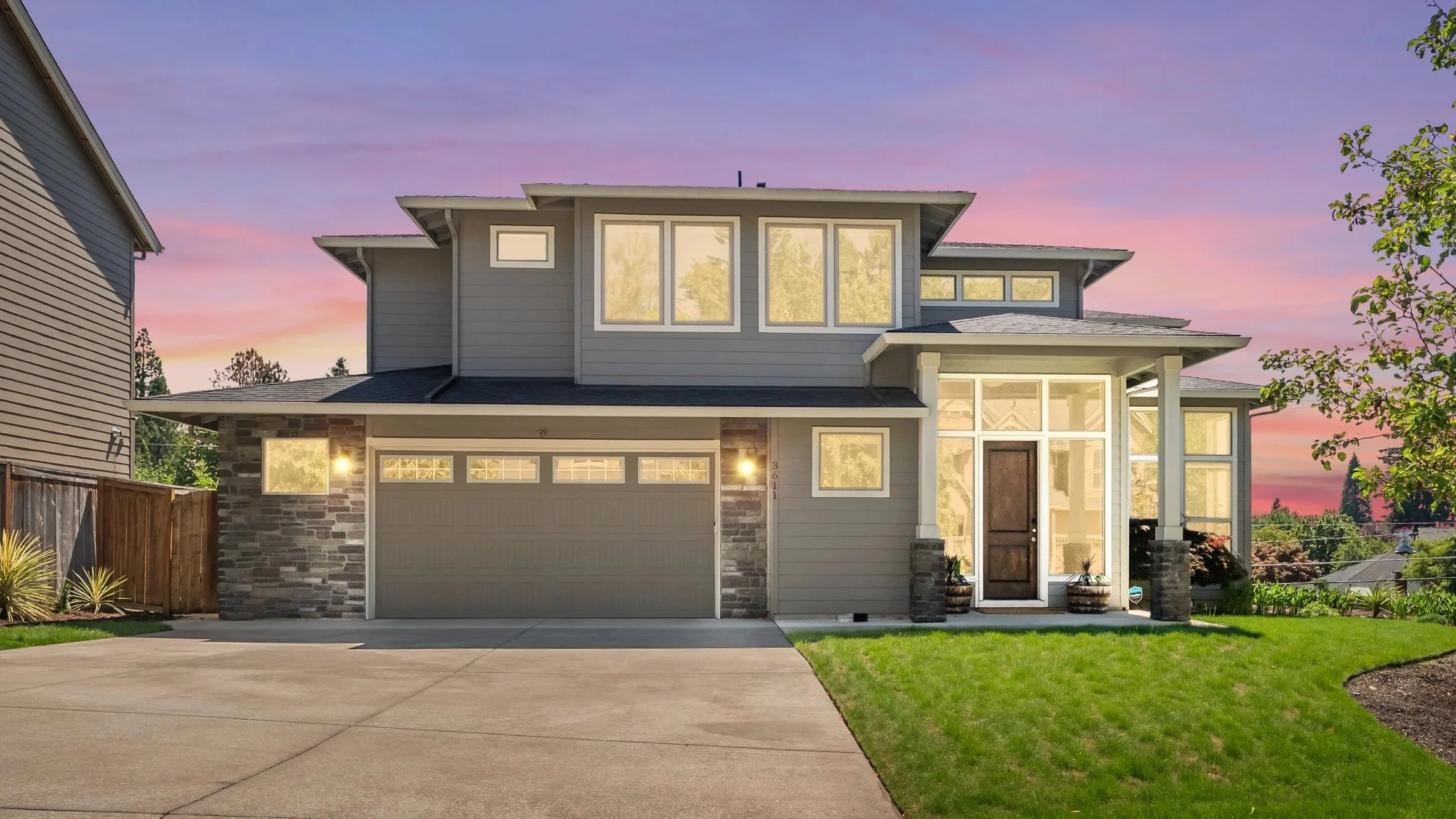 Modern two-story house with a stone and siding exterior, large windows, attached garage, front door, and a well-maintained lawn at sunset.