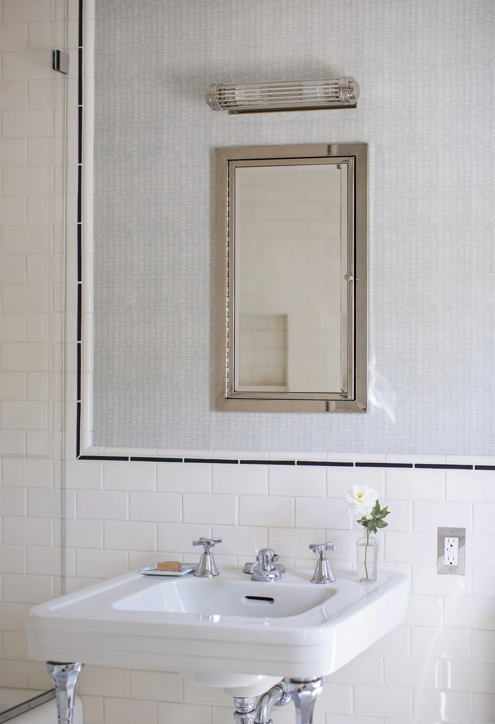 Guest bath with a white pedestal sink, a nickel medicine cabinet, subway tile with a navy border and a single flower in a bud vase