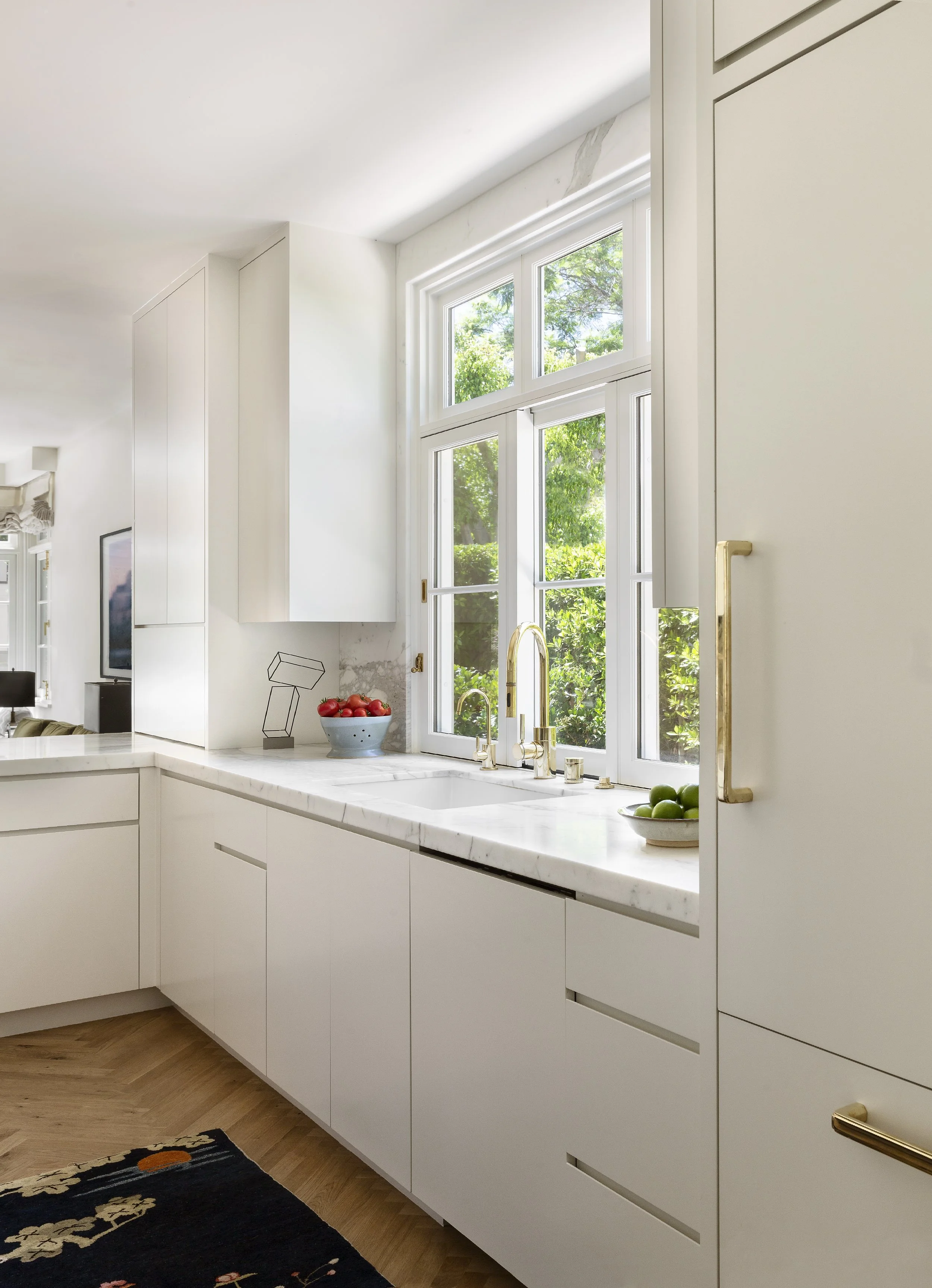 Kitchen corner with a window over the sink, white cabinetry and brass pulls