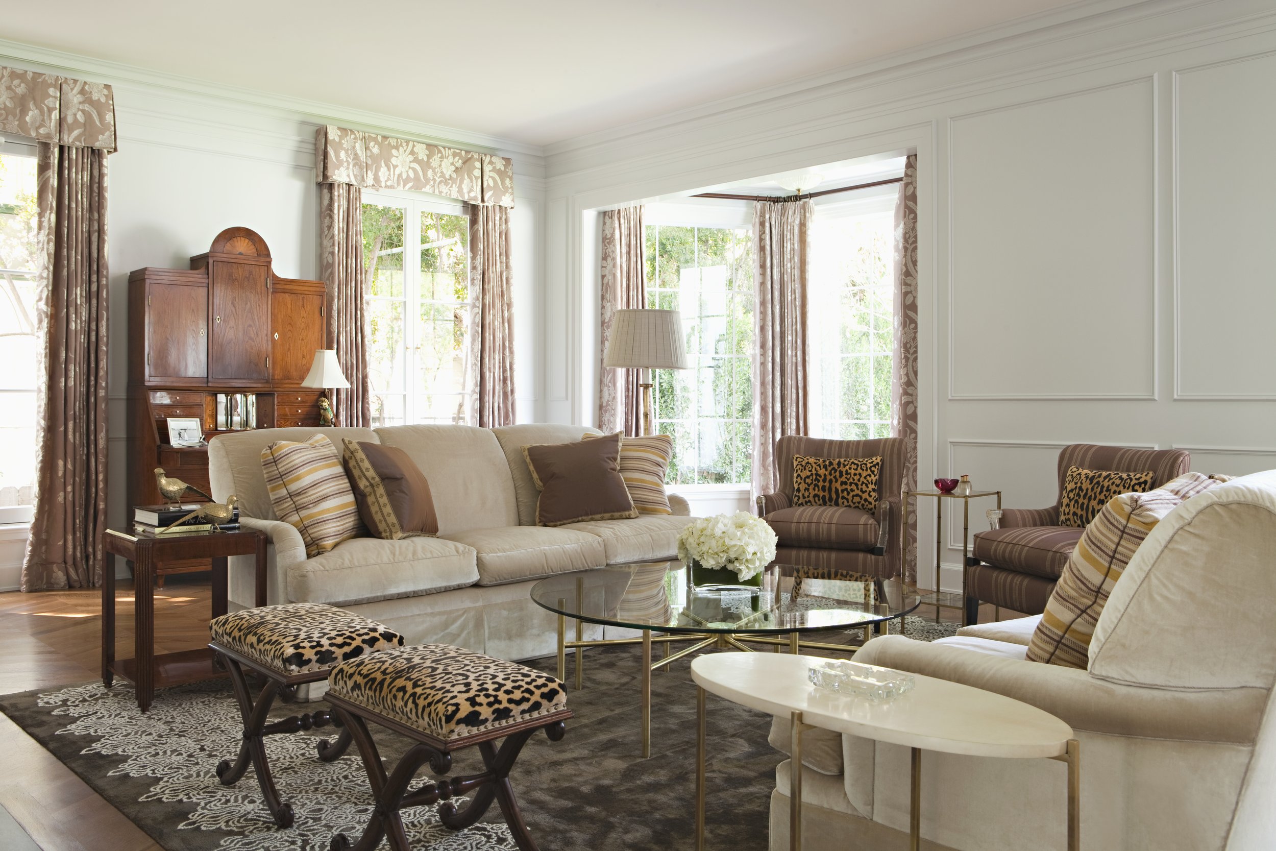 Living room with white paneled walls, a cream sofa, leopard ottomans and a glass coffee table