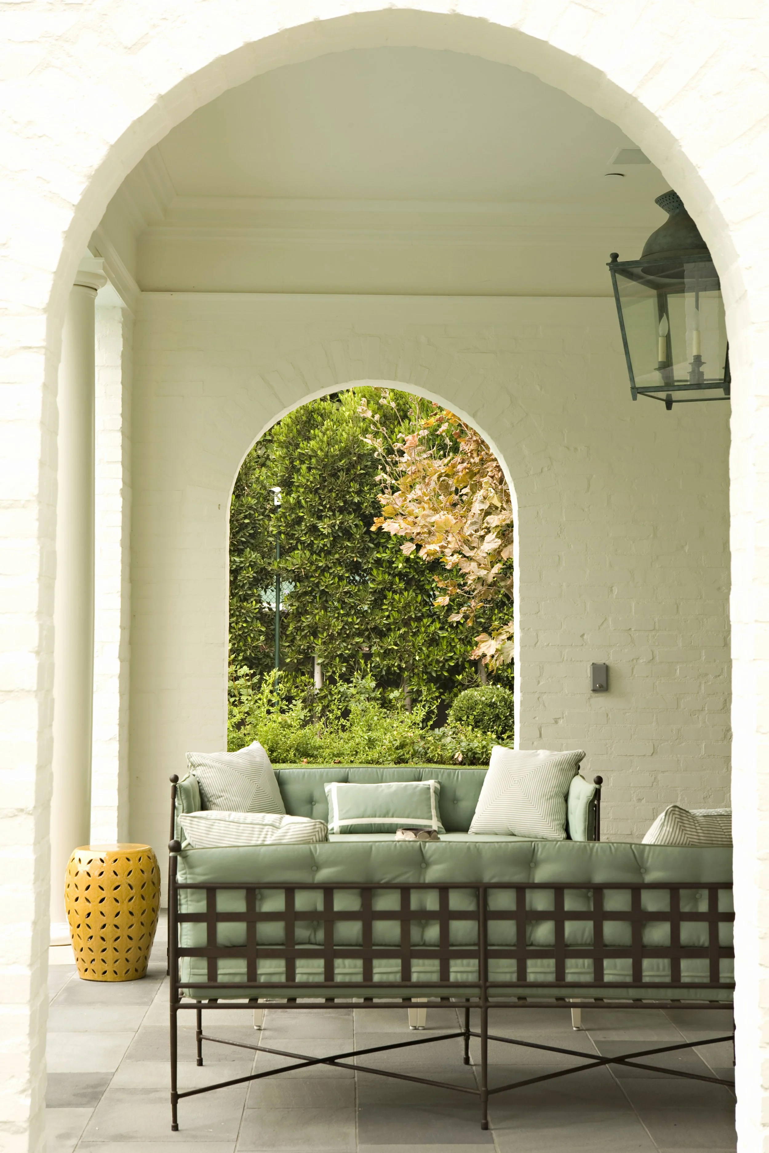 Arched opening in a white brick wall framing a garden, with a sofa below