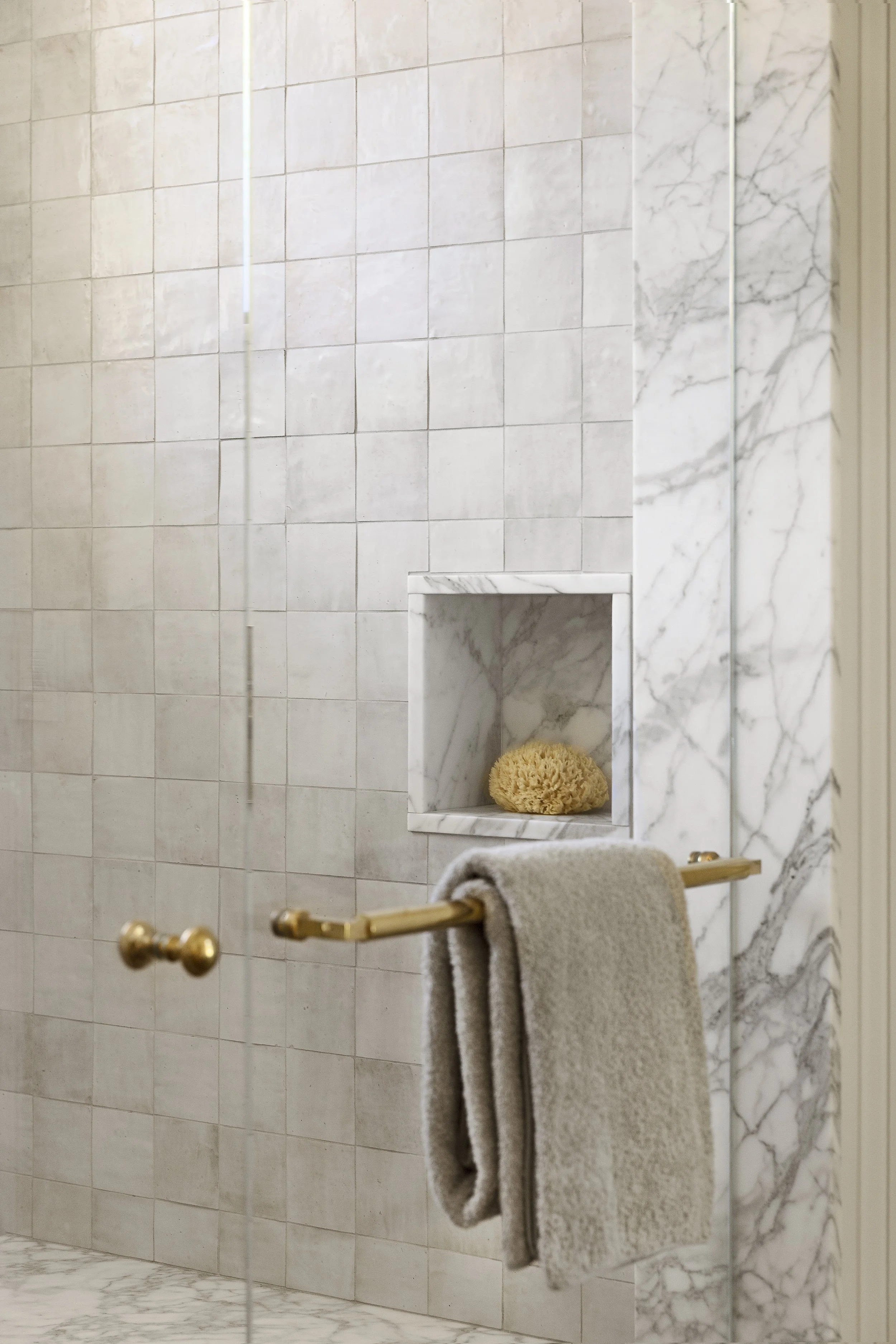 Marble shower wall with a niche, brass towel bar and gray towel