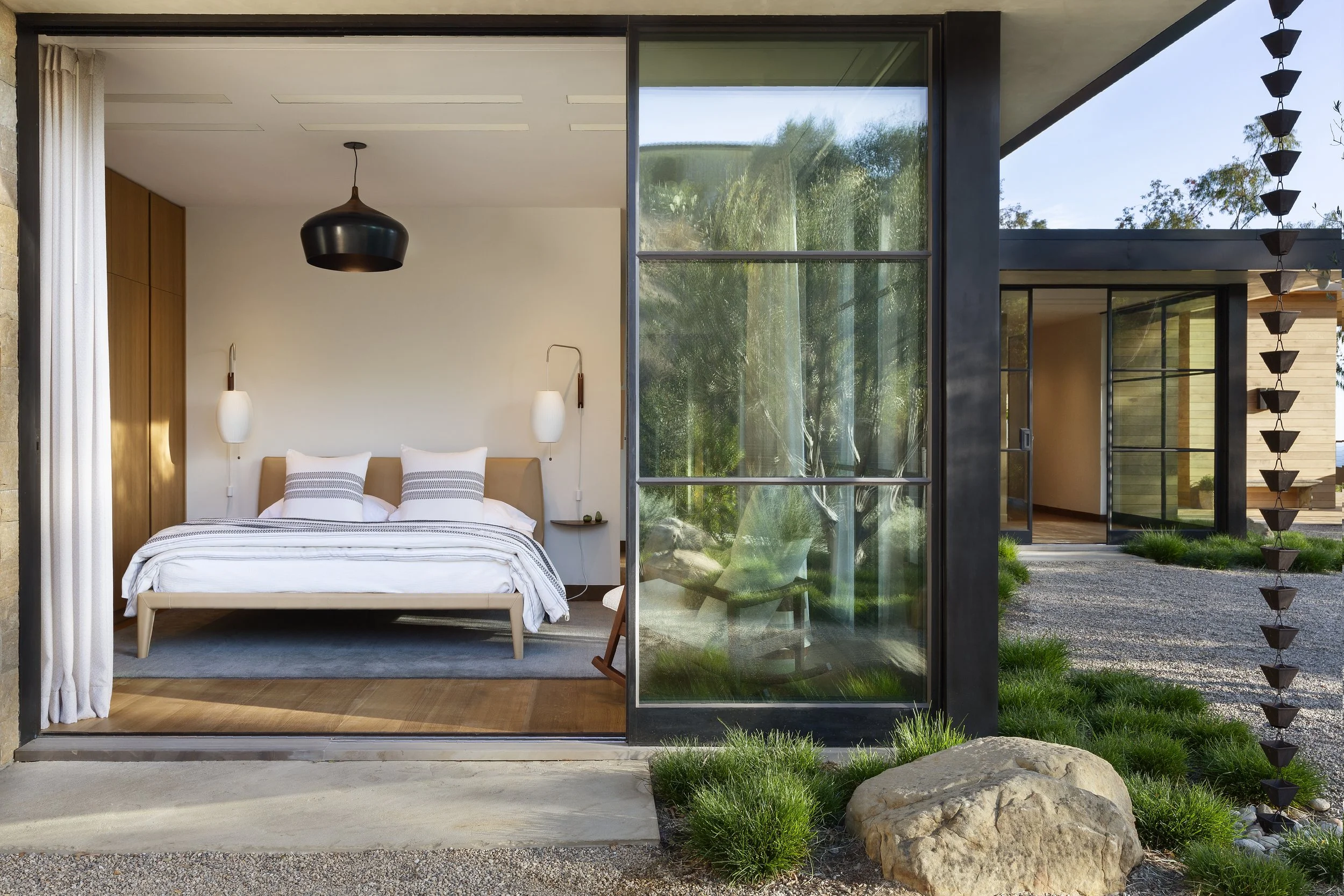 Bedroom with a black pendant and a steel-framed glass wall opening to the garden