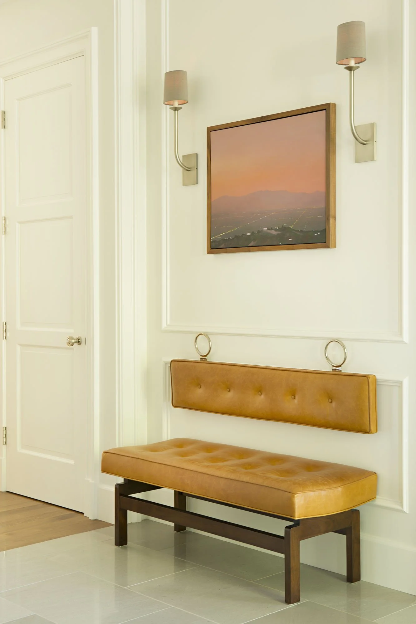 Tufted tan leather bench beneath a framed sunset landscape